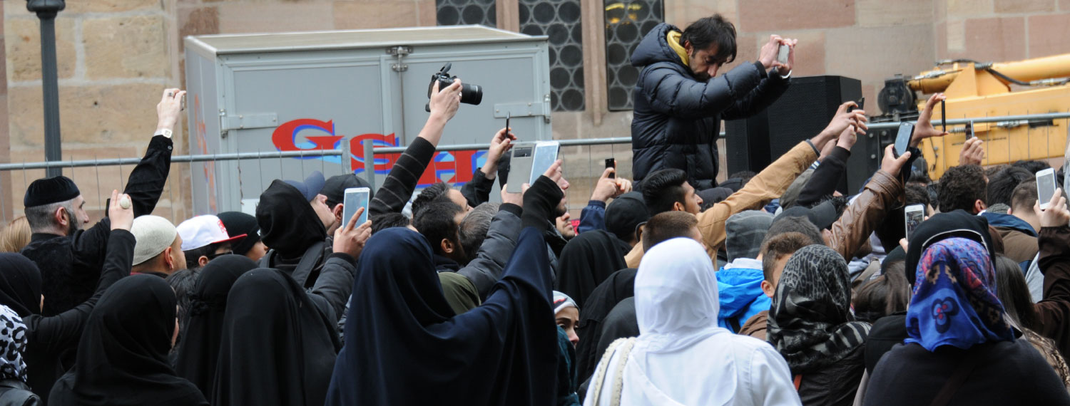 Gruppe von Männern und Frauen, teilweise islamisch gekleidet, die etwas fotografieren.